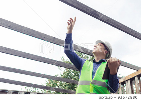 Building inspector. Man in a hard hat and a yellow reflective vest examines damaged structures and inspects the building. Damage assessment. Preparing for the repair or construction of a building Building inspector. Man in a hard hat and a yellow reflective vest examines damaged structures and inspects the building. Damage assessment. Preparing for the repair or construction of a building 93672880