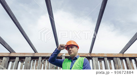 Building inspector. Man in a hard hat and a yellow reflective vest examines damaged structures and inspects the building. Damage assessment. Preparing for the repair or construction of a building Building inspector. Man in a hard hat and a yellow reflective vest examines damaged structures and inspects the building. Damage assessment. Preparing for the repair or construction of a building 93672884
