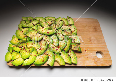 Avocado slices on a wooden textured background sprinkled with spices, bright accent. View from above 93673203