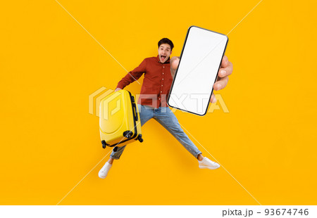 Excited Tourist Guy Jumping With Luggage And Showing Big Blank Smartphone Excited Tourist Guy Jumping With Luggage And Showing Big Blank Smartphone 93674746