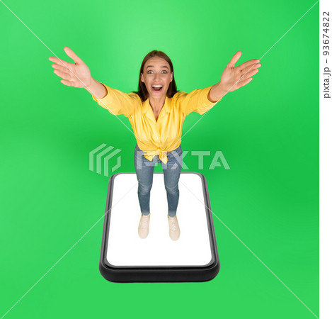 Excited Woman Standing On Huge Smartphone Screen Over Green Background Excited Woman Standing On Huge Smartphone Screen Over Green Background 93674822