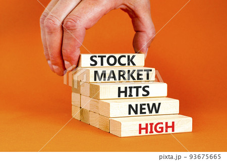 Stock market hits new high symbol. Concept words Stock market hits new high on wooden blocks on a beautiful orange background. Businessman hand. Business stock market hits new high concept. Copy space Stock market hits new high symbol. Concept words Stock market hits new high on wooden blocks on a beautiful orange background. Businessman hand. Business stock market hits new high concept. Copy space 93675665