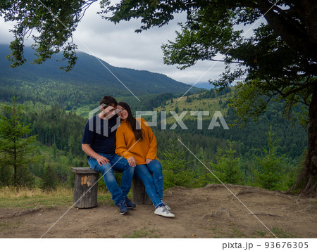 Couple in casual clothes sit under large tree with forest background Couple in casual clothes sit under large tree with forest background 93676305