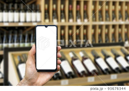 Wine shop with bottles background. Hand with blank smartphone screen one wine backdrop. Buying and ordering alcoholic beverages online 93676344