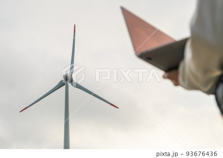 Close up woman uses a laptop to control the work of the windmill against the grey sky. Close up woman uses a laptop to control the work of the windmill against the grey sky. 93676436