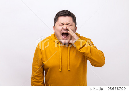Angry nervous middle aged man loudly yelling widely opening mouth holding hands on face, screaming announcing his opinion, wearing urban style hoodie. Indoor studio shot isolated on white background. 93678709