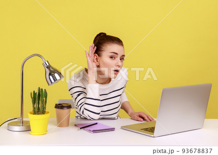 I can't hear you. Woman manager holding arm near ear trying to listen secret while working online on laptop in home office. Indoor studio studio shot isolated on yellow background. I can't hear you. Woman manager holding arm near ear trying to listen secret while working online on laptop in home office. Indoor studio studio shot isolated on yellow background. 93678837
