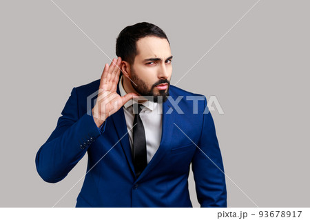 Concentrated nosy bearded man holding hand near ear, listening to interesting talks and private secrets, spying, wearing official style suit. Indoor studio shot isolated on gray background. Concentrated nosy bearded man holding hand near ear, listening to interesting talks and private secrets, spying, wearing official style suit. Indoor studio shot isolated on gray background. 93678917