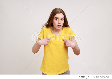 This is me. Amazed attractive teenager girl with brown hair pointing to herself with wondered expression, surprised by own success, disbelief reaction. Indoor studio shot isolated on gray background. 93678928