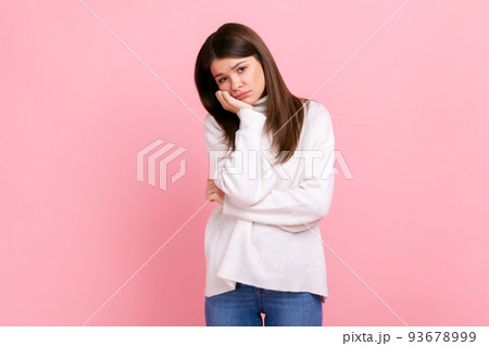 Bored girl look at camera with an incredulous, disappointed emotions on face and hand near her head, wearing white casual style sweater. Indoor studio shot isolated on pink background. 93678999