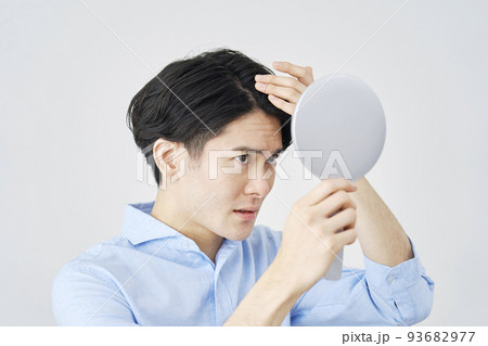 白背景でハンドミラーを持って髪の毛を見る男性 93682977