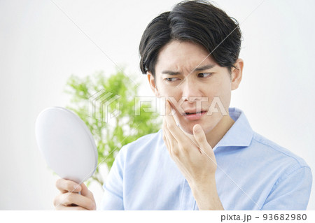 自宅でハンドミラーを持って顔を見る男性 93682980