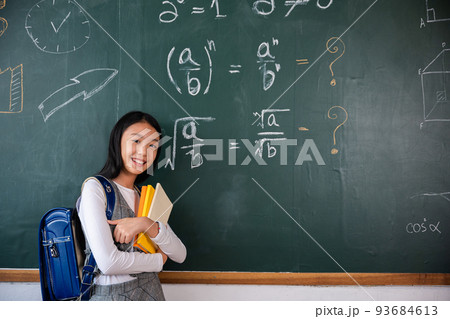 Happy beautiful Asian Schoolgirl girl standing holding books standing in front blackboard of classroom Happy beautiful Asian Schoolgirl girl standing holding books standing in front blackboard of classroom 93684613