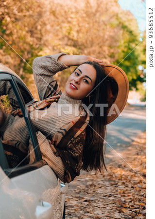 Brunette European looking cute girl sitting in a car enjoying sunny autumn weekend. Travel and road trip. Woman looking at the view from a car. Happy woman enjoying road trip 93685512