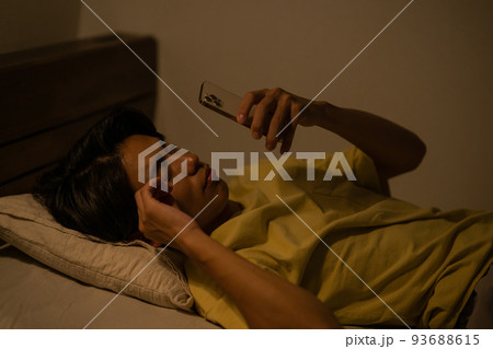 睡眠・寝室のベッドでウトウトしながらスマホを見る男性イメージ 93688615