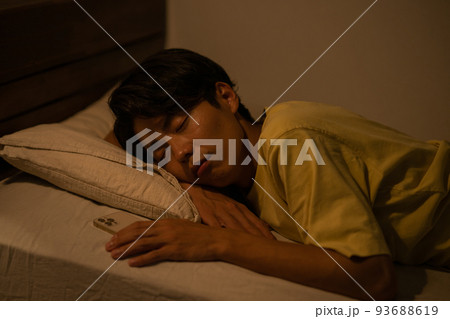 睡眠・寝室のベッドでスマホを握りながら眠る男性イメージ 93688619