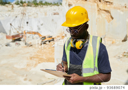 Young engineer in workwear making notes in working document in clipboard 93689074