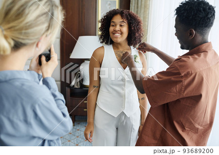 Happy young African American bride posing in front of bridesmaid with smartphone 93689200