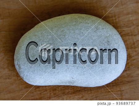 Capricorn zodiac sign text engraved on a stock with wooden background. Zodiac sign concept. 93689737