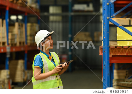 Young woman warehouse worker in hardhats and reflective jackets using digital tablet and counting boxes on shelf Young woman warehouse worker in hardhats and reflective jackets using digital tablet and counting boxes on shelf 93689914