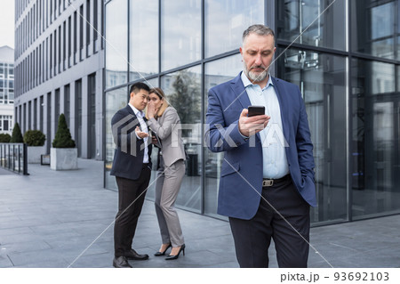 Two colleagues are gossiping at background behind the boss. workmate about bullying problem at work place in office in the break outside Male Coworkers employees man and woman Whispering Behind Back. Two colleagues are gossiping at background behind the boss. workmate about bullying problem at work place in office in the break outside Male Coworkers employees man and woman Whispering Behind Back. 93692103