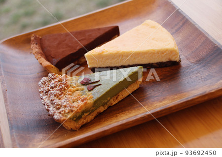 抹茶のタルト、チーズケーキ、ショコラタルト、アカシアの皿に盛り付けられた焼菓子 抹茶のタルト、チーズケーキ、ショコラタルト、アカシアの皿に盛り付けられた焼菓子 93692450