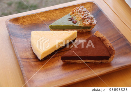 抹茶のタルト、チーズケーキ、ショコラタルト、アカシアの皿に盛り付けられた焼菓子 93693323