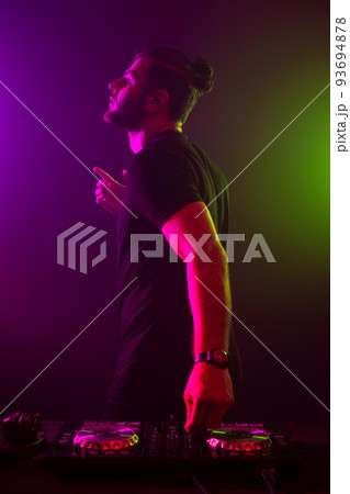 Attractive young DJ playing on turntables with color light effects 93694878