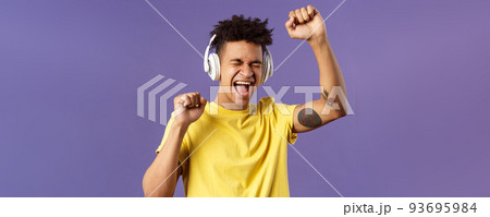 Close-up portrait of cheerful, happy young dancing guy lift hand up singing along, close eyes and smiling upbeat as listening awesome song in headphones, enjoying music, purple background Close-up portrait of cheerful, happy young dancing guy lift hand up singing along, close eyes and smiling upbeat as listening awesome song in headphones, enjoying music, purple background 93695984