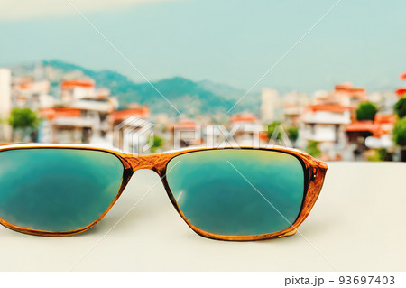 Sunglasses on a white table on the background of a seaside city on a sunny day Sunglasses on a white table on the background of a seaside city on a sunny day 93697403