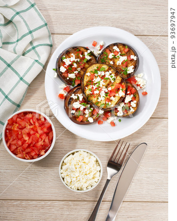 Homemade grilled eggplant with feta and tomatoes on a white table, top view. 93697947