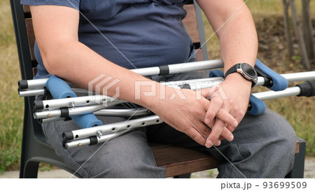 Man sitting with folded crutches in the park Man sitting with folded crutches in the park 93699509