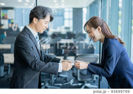 オフィスで名刺交換をするベテラン男性と若い女性 93699799