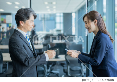 オフィスで名刺交換をするベテラン男性と若い女性 93699800