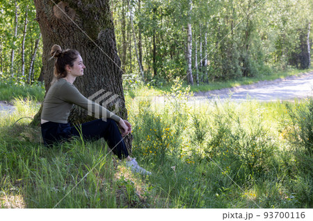 Young brunette woman sitting in green forest enjoys the silence and beauty of nature watching over a Young brunette woman sitting in green forest enjoys the silence and beauty of nature watching over a 93700116