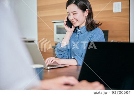 テレワーク中にスマホで電話をする若い女性 93700604