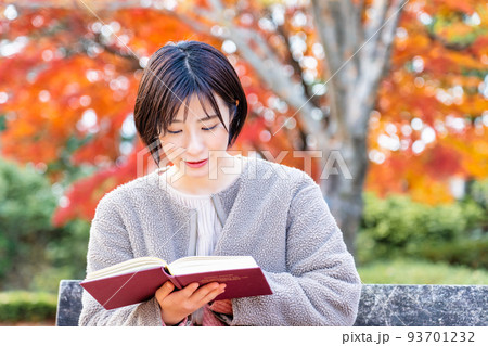 紅葉の公園のベンチで読書をする若い女性 93701232