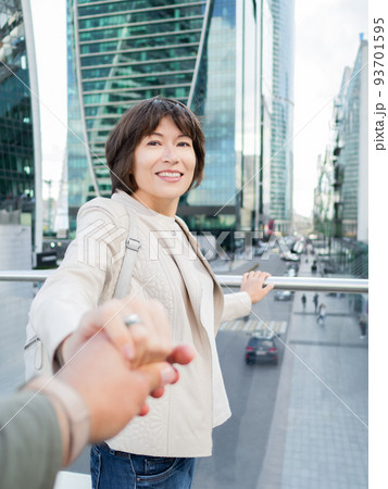 Man leads smiling woman by hand against  background of glass walls of modern buildings. Downtown with skyscrapers and finance business centers. Urban lifestyle. 93701595