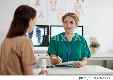 Young female doctor talking to female patient and writing down disease symptoms Young female doctor talking to female patient and writing down disease symptoms 93702553