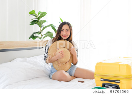 Portrait of young Asian woman in summer casual clothes and straw hat smiling and relaxing mood with yellow baggage in bedroom. It time to go to travel in summer time. Happy tourist woman with yellow 93702566