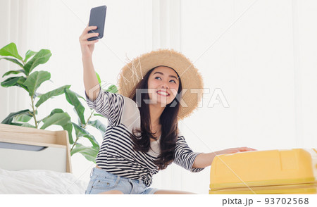 Young Asian woman blogger smiling in summer casual clothes and straw hat talking to facetime video calling with smartphone in bedroom. 93702568