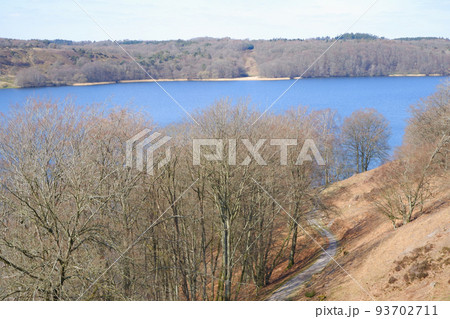 Landscape in early spring. A beautiful lake surrounded by hills with trees without leaves. Early spring. Spring landscape with trees by the river Landscape in early spring. A beautiful lake surrounded by hills with trees without leaves. Early spring. Spring landscape with trees by the river 93702711