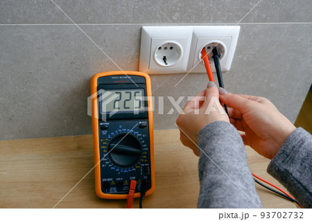Woman with a multimeter check the voltage of the electrical network. woman checking voltage in power socket. Close-up view of the hands with the appliance near the socket. 93702732