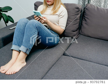 A woman at home sitting on the couch communicates with relatives via video call using a smartphone. Young woman making video call with her family A woman at home sitting on the couch communicates with relatives via video call using a smartphone. Young woman making video call with her family 93702761