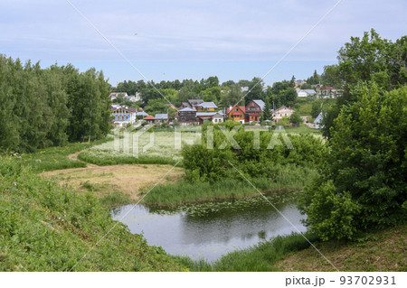 View of the pond, blooming meadow, forest and cottages in summer in Suzdal, Russia 93702931