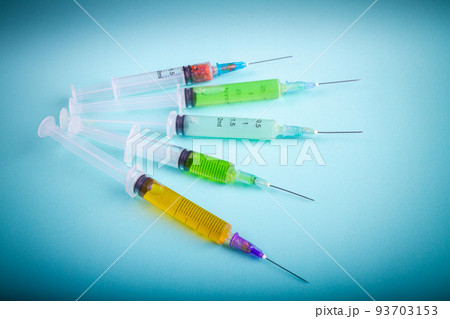 Several various syringes with multicolored medicine on blue background. Drugs or vaccine injections. 93703153