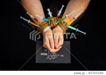 Many colorful syringes sticking from bound male hands. Isolated on black background. Many colorful syringes sticking from bound male hands. Isolated on black background. 93703160