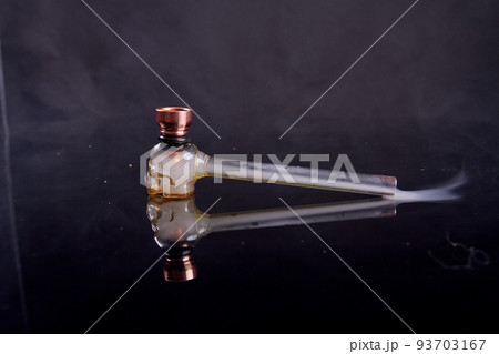 Glass pipe for crack or crystal meth on reflective mirror surface. Smoke on black background. Glass pipe for crack or crystal meth on reflective mirror surface. Smoke on black background. 93703167