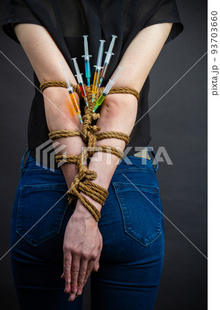 Back view young girl with bound arms and stucked syringes. Drug dependence and addiction concept. Back view young girl with bound arms and stucked syringes. Drug dependence and addiction concept. 93703660