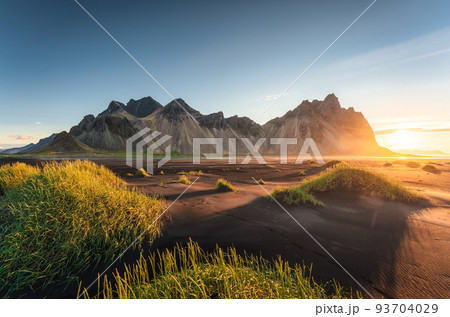 Sunrise over Vestrahorn mountain and clump of grass on black sand beach in Stokksnes on the southeastern at Iceland Sunrise over Vestrahorn mountain and clump of grass on black sand beach in Stokksnes on the southeastern at Iceland 93704029